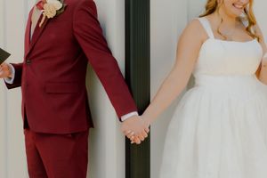 Bride and groom holding hands in wedding attire, groom in burgundy suit and bride in white dress.