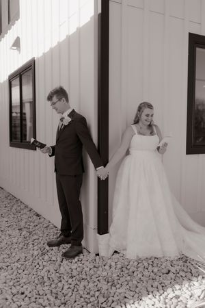 Black and white photo of bride and groom reading vows privately separated by a corner wall.