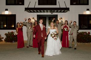 Bride and groom walk together as wedding party celebrates behind them outside illuminated white venue.