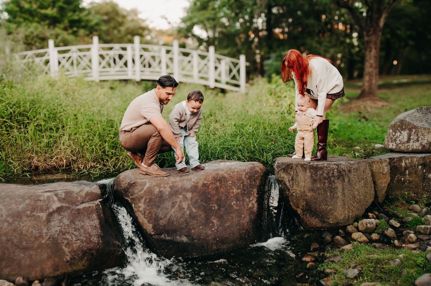 Playful couple posing on rocky waterfall ledge during outdoor photo session.