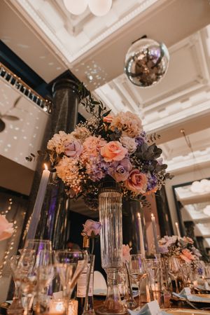 Elegant floral centerpieces with pink and purple blooms cascade over crystal vases at a luxurious wedding reception.