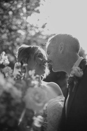 Romantic black and white portrait of a couple getting close in dappled sunlight through trees.