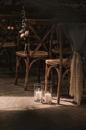 Rustic wooden chairs with flickering candle lanterns create an intimate atmosphere in a dimly lit wedding venue setting.