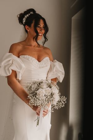 A bride in an elegant white off-shoulder gown holds a delicate bouquet of baby's breath flowers.