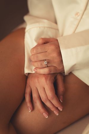 Close-up view of hands with diamond engagement ring resting on a smooth beige surface involving romantic composition.