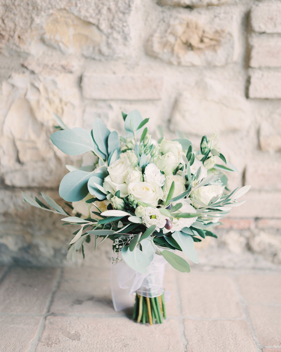 Tuscany bridal bouquet with olive tree leafs, white roses, and some eucalyptus leafs, leaning on a typical old wall of a Italian farmhouse