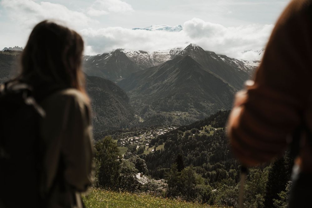 Two people admiring an alpine mountain valley from above — summer outdoor lifestyle photography in the French Alps — Paul Brechu