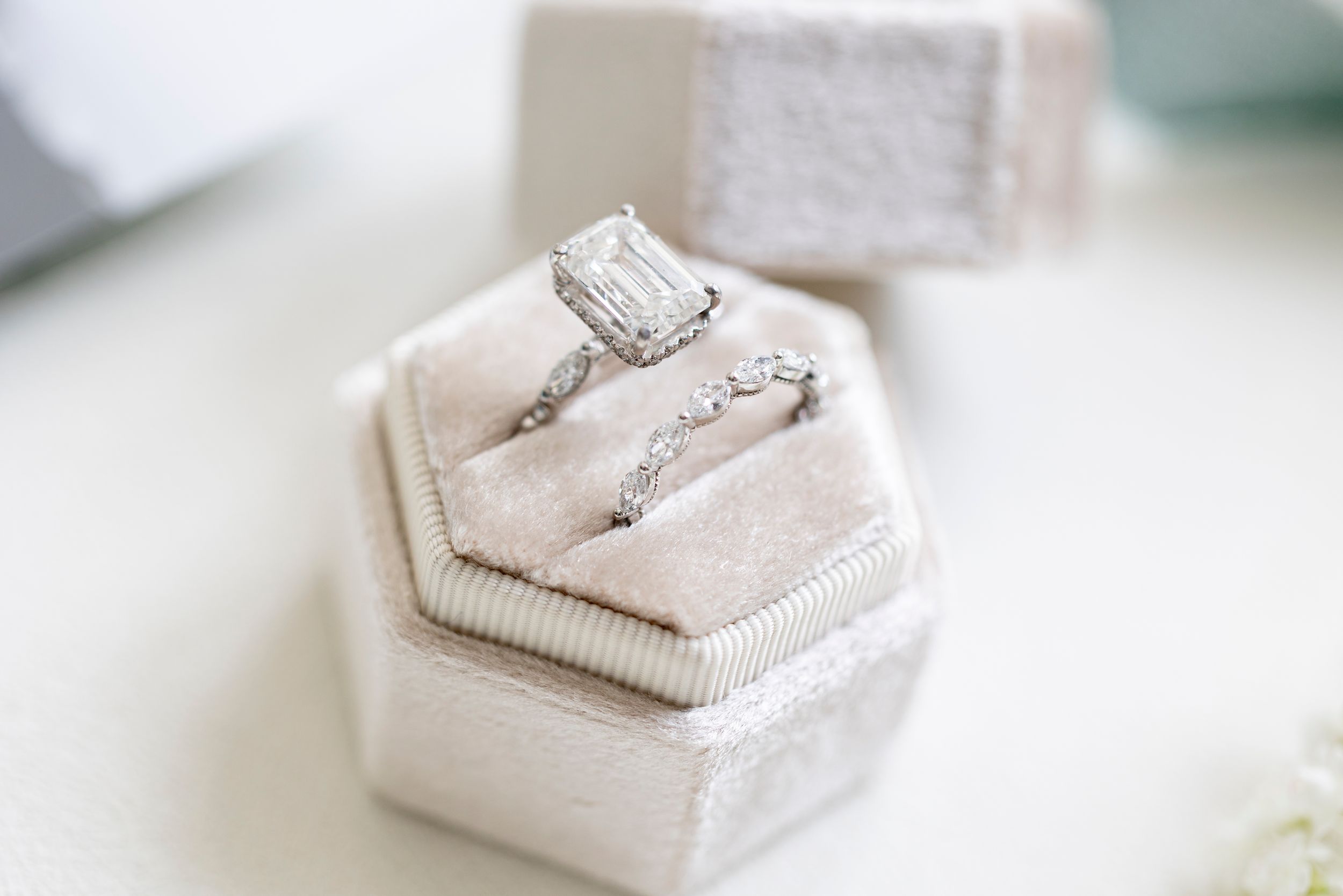 Sparkling diamond engagement ring and wedding band nestled in a cream velvet hexagonal ring box.