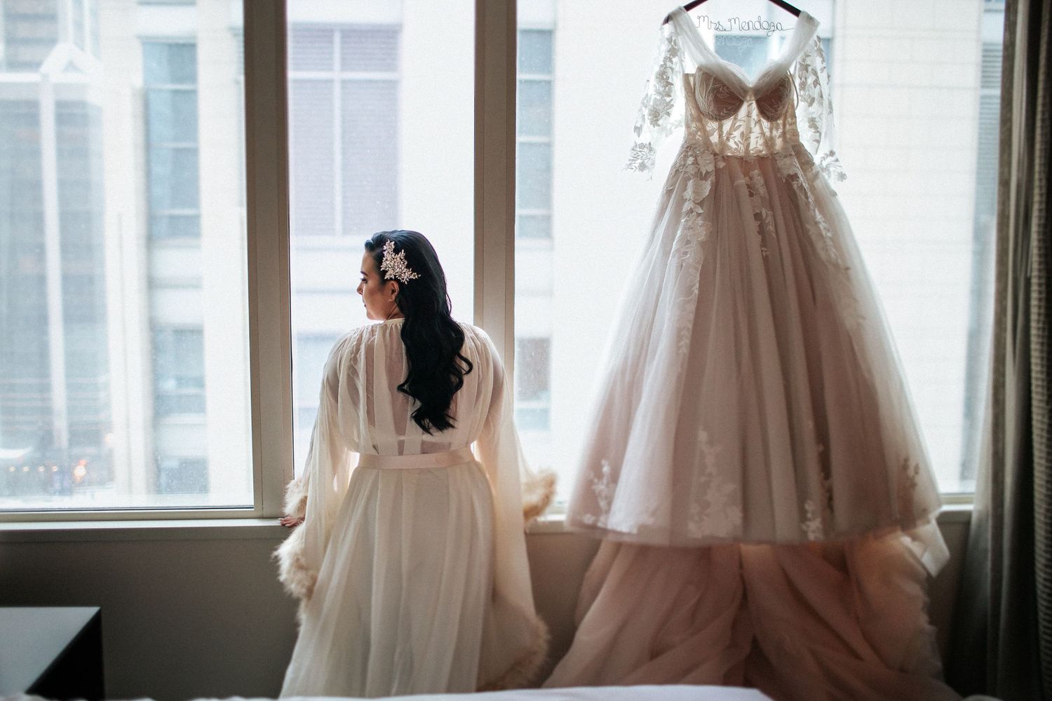 Elegant wedding dresses displayed on hangers by a bright window in a bridal boutique.