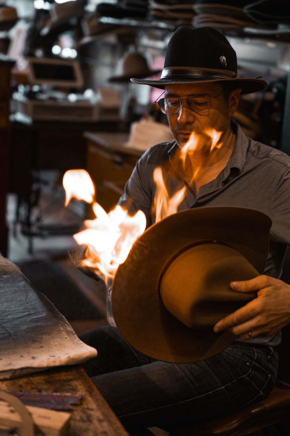 A craftsman shapes a felt cowboy hat over open flames in a traditional hat-making workshop.