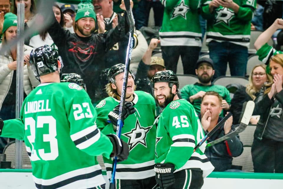 Dallas Stars players celebrate a goal during an NHL hockey game with fans cheering in the background.