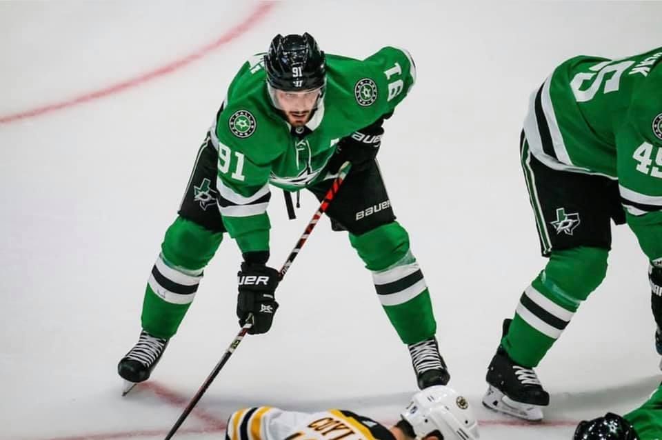 NHL hockey player in green Dallas Stars jersey handles puck during game action.