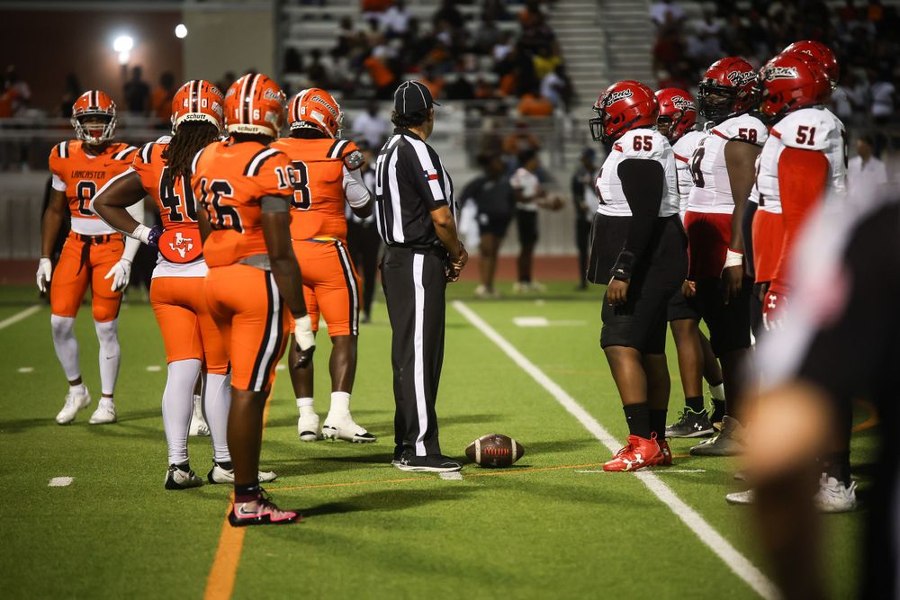 Football teams in orange and dark uniforms line up on the field during a nighttime game.