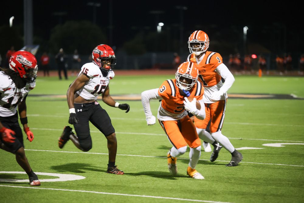 Players in orange uniforms tackle during a nighttime football game.