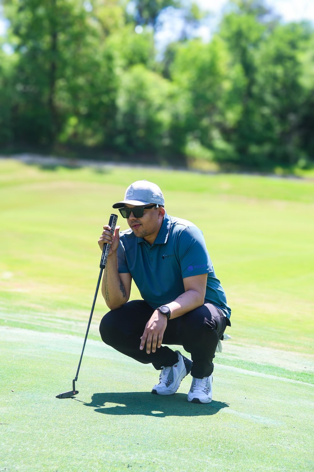 A golfer crouches down to read the green and analyze the putting line during a round of golf.