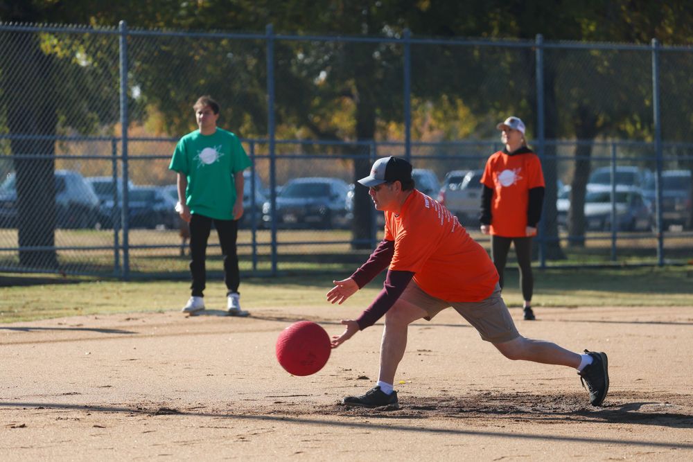 Players in colorful shirts playing kickball on outdoor field during sunny day.