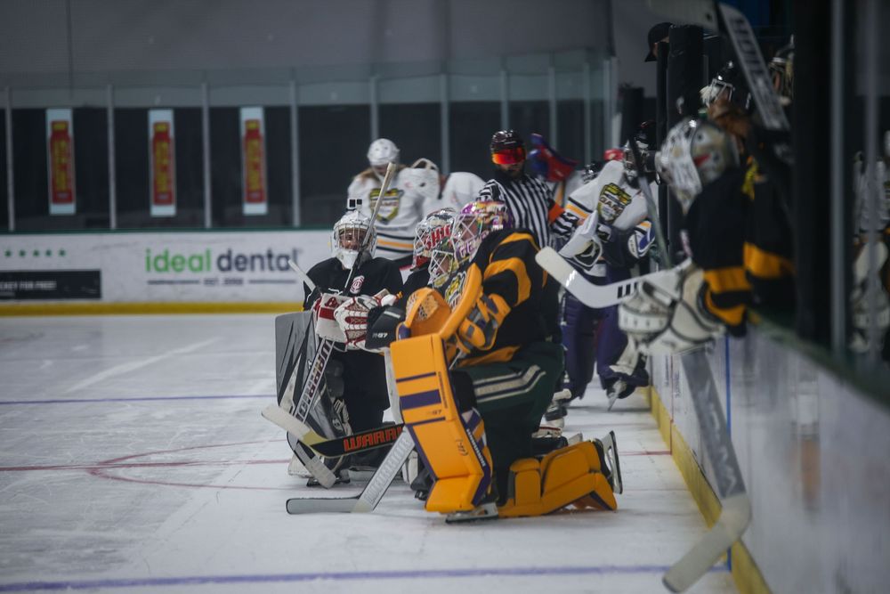 Hockey players collide on the ice during an intense game with yellow and white jerseys visible.
