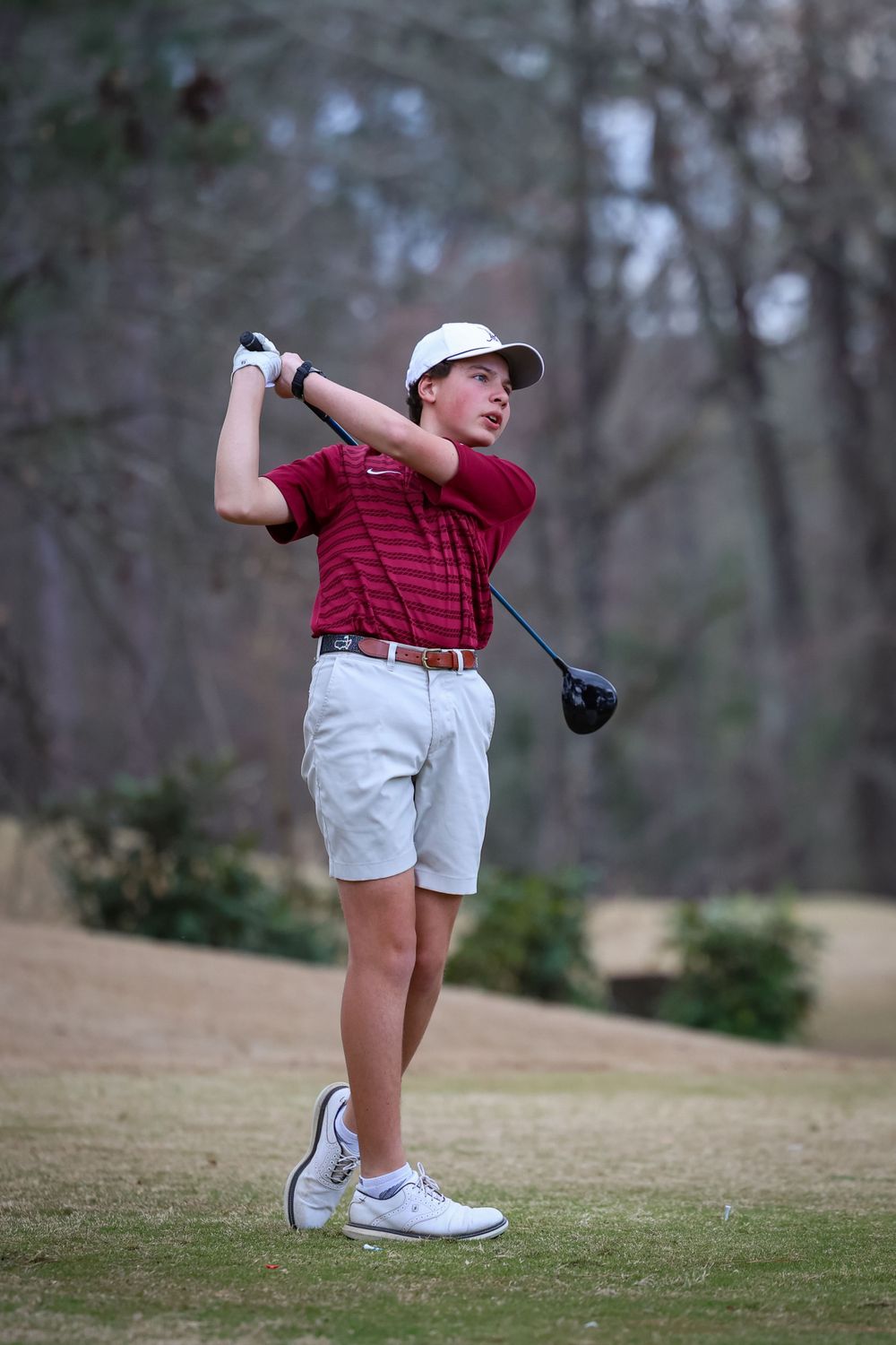 Young golfer in red striped shirt taking a swing with driver on golf course.