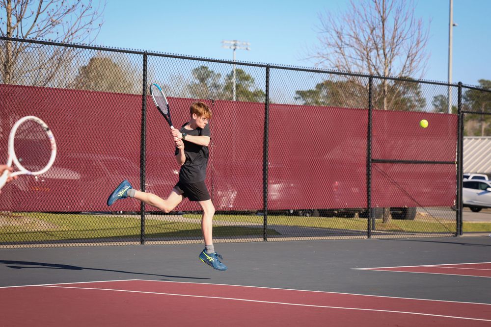 Tennis player jumping to return shot on outdoor court.