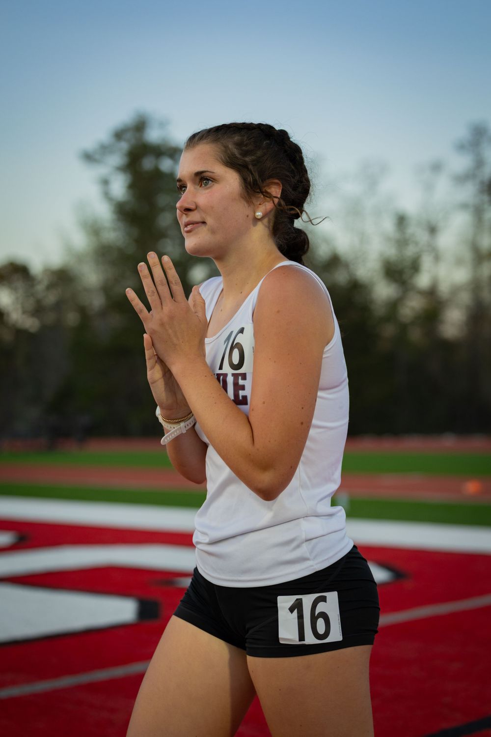Track athlete in white uniform clasps hands while competing at sunset.