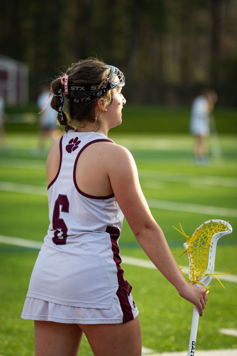 Lacrosse player in white uniform holds yellow stick on sports field.