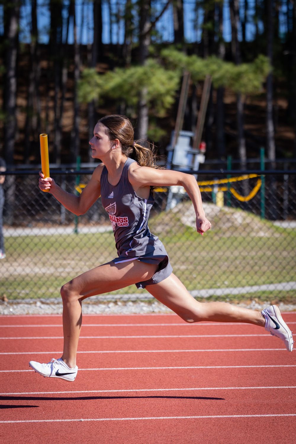 Track athlete running with baton during relay race on outdoor track.