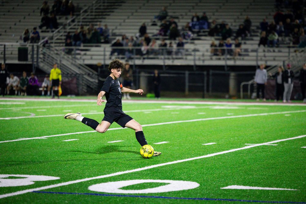Soccer player kicking ball on illuminated field during nighttime game.