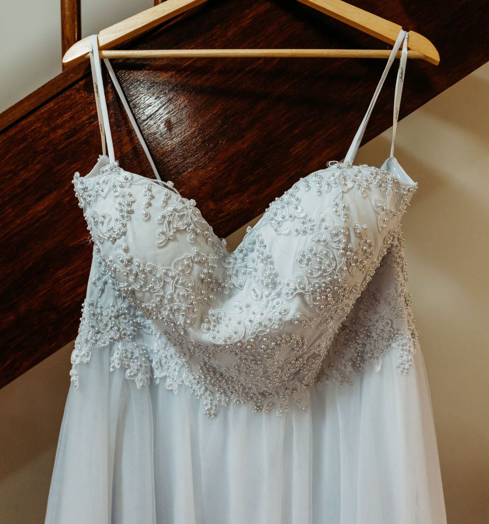 Delicate white wedding dress with lace bodice hanging on wooden hanger.