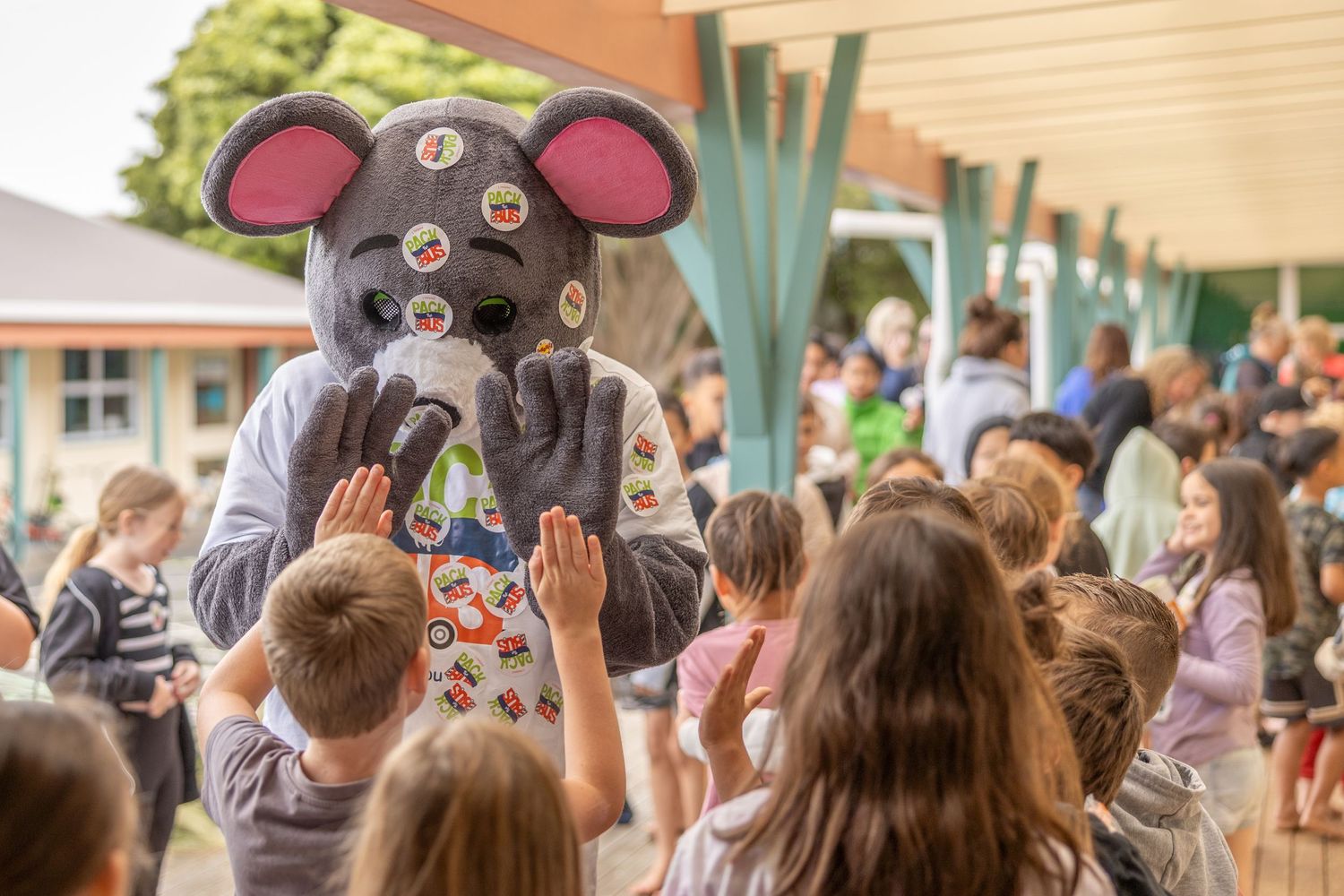A person in a mouse mascot costume entertains a crowd of children at an outdoor event.