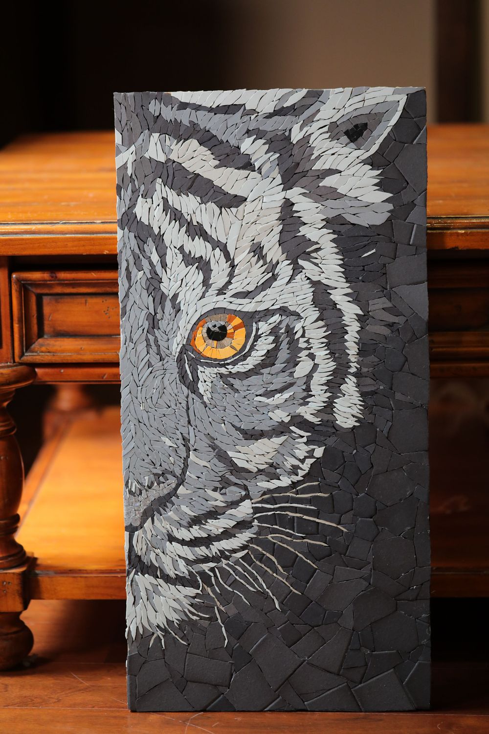 Black and grey mosaic art piece depicting a tiger's piercing yellow eye and partial face against a dark background.