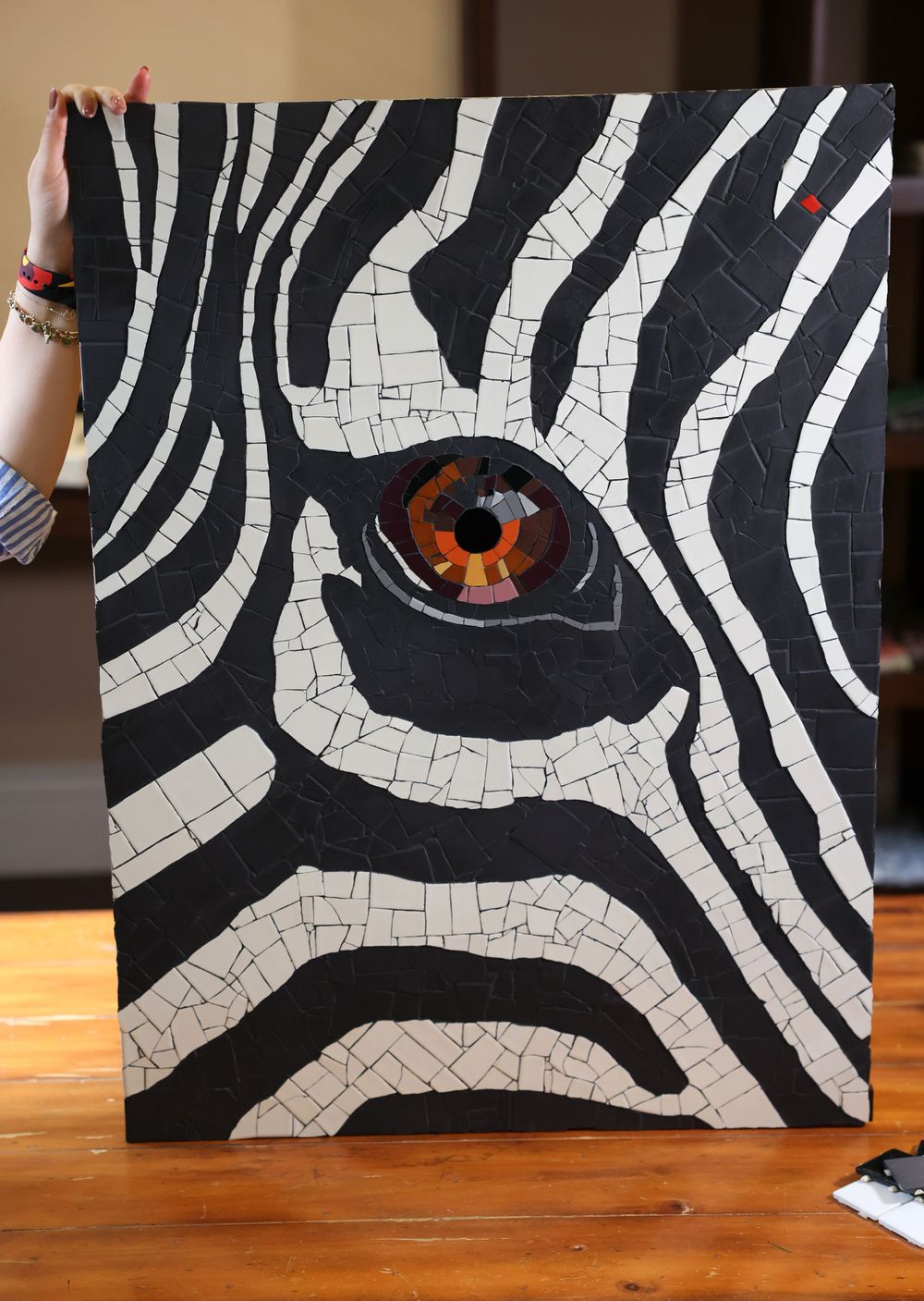 A striking mosaic artwork depicts a black and white zebra pattern with an orange eye detail against a dark background.