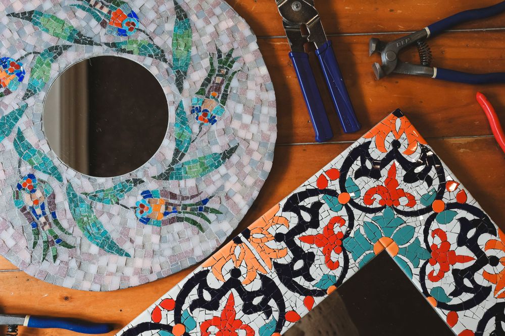 Colorful mosaic art pieces with floral patterns alongside crafting tools on a wooden surface.