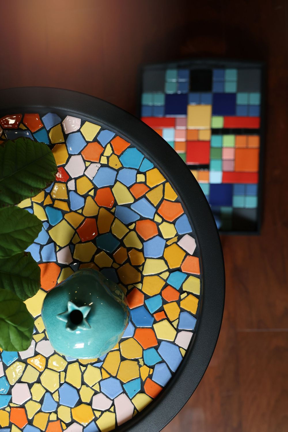 Colorful mosaic table detail with stained glass pattern beside a blue pumpkin and digital pixel art display in background.