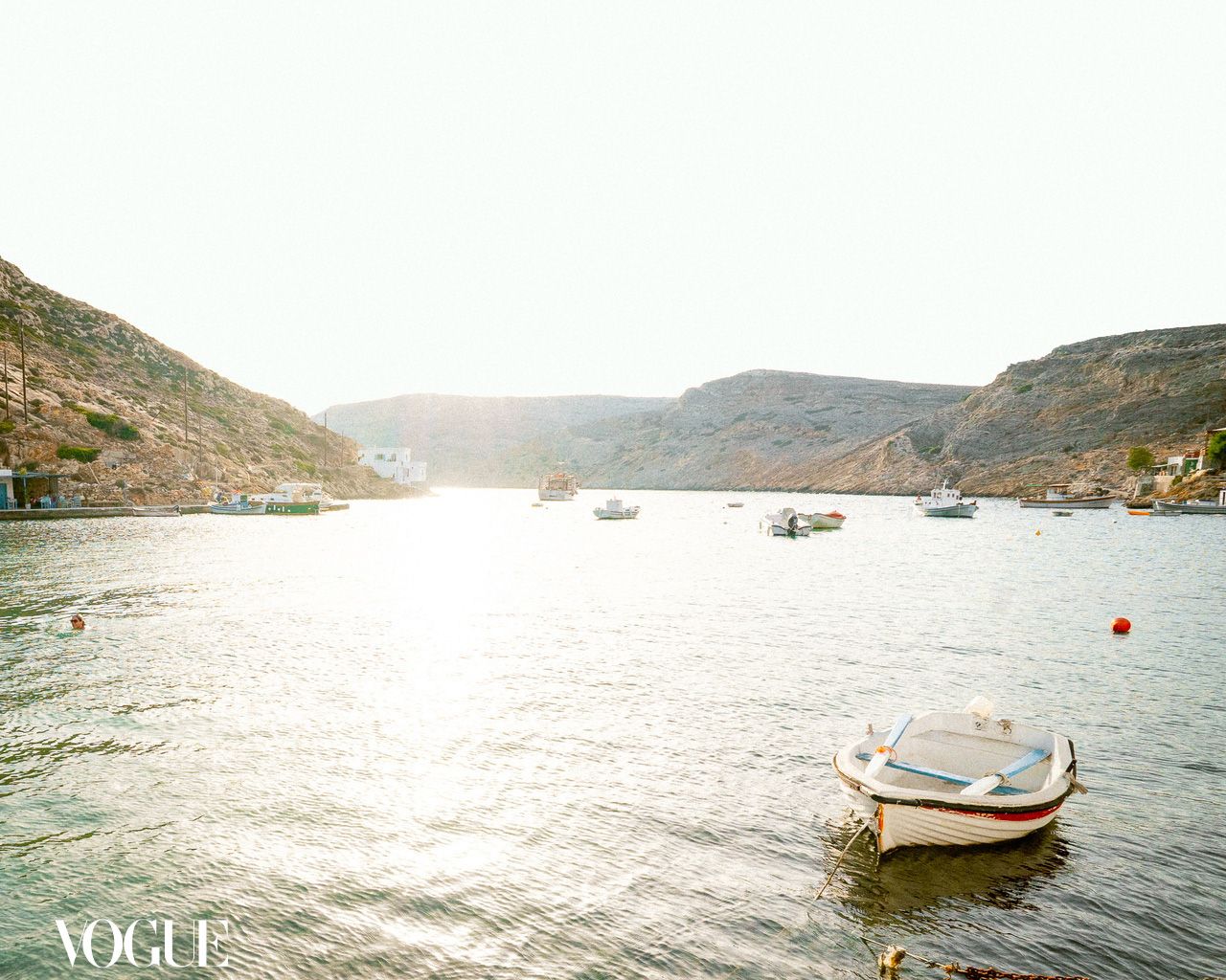 Small boat floating on calm coastal water between hills in seaside landscape.