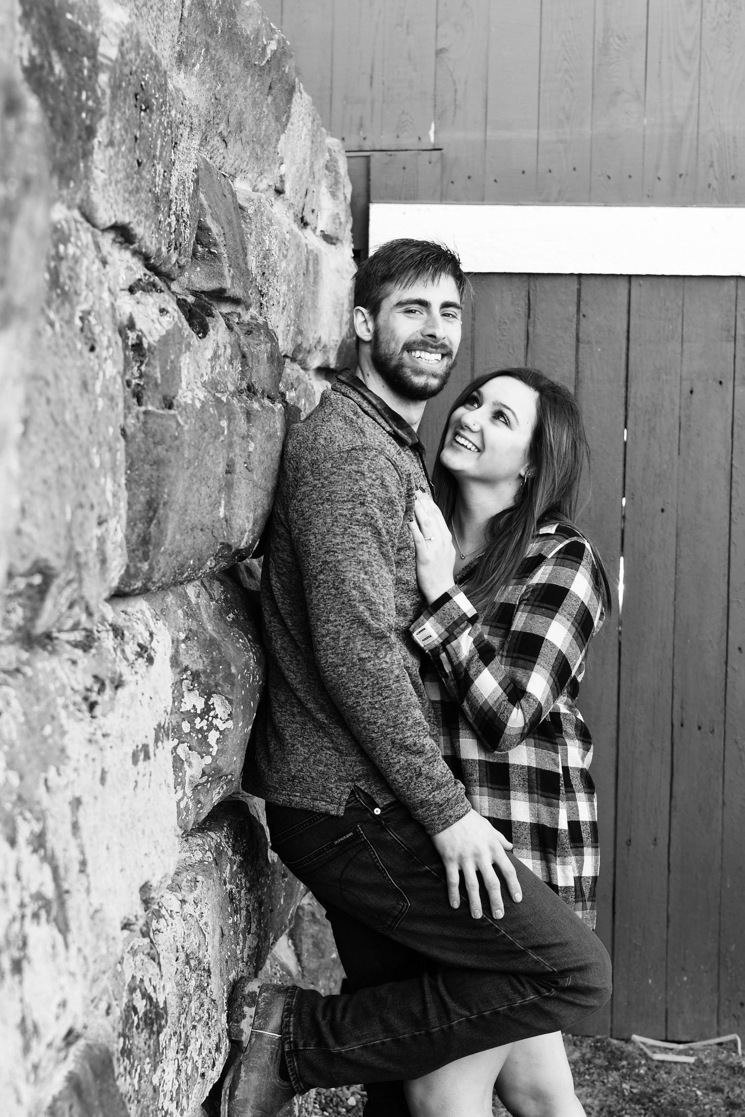 Black and white portrait of couple embracing against rustic stone wall and wooden door.