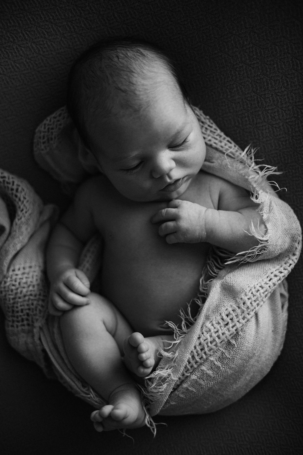 Artistic black and white photo of infant wrapped in textured fabric.