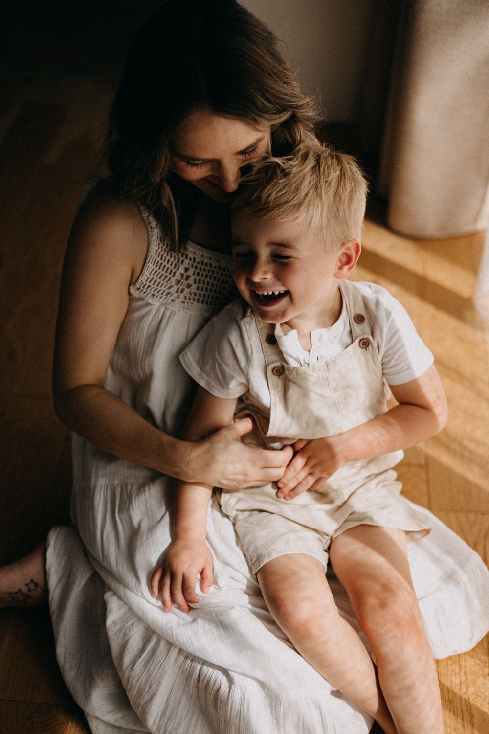 A tender moment of laughter and joy shared between a parent and child sitting together on a wooden floor.