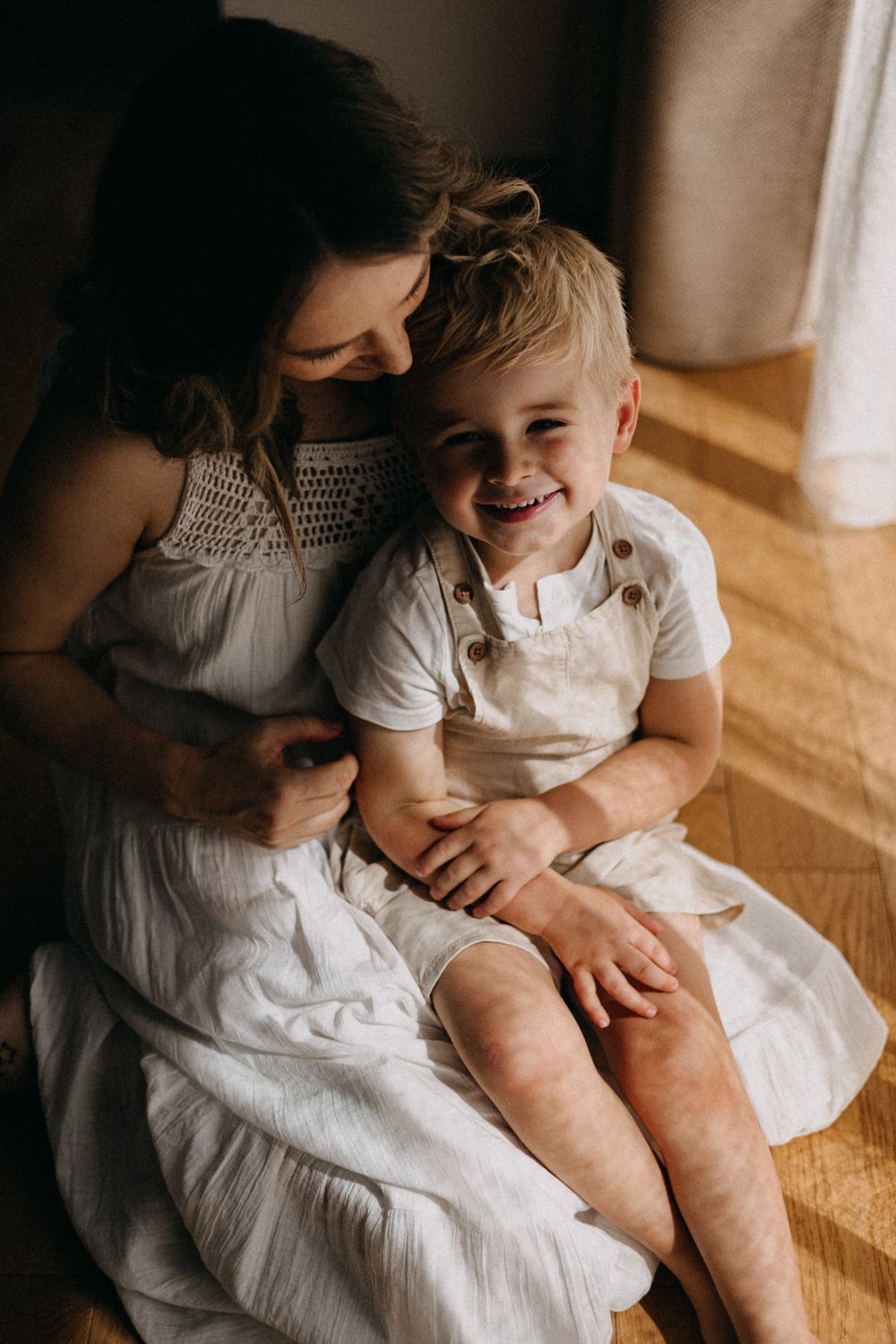Intimate portrait of a parent and child sharing cheerful laughter while sitting in natural window light.