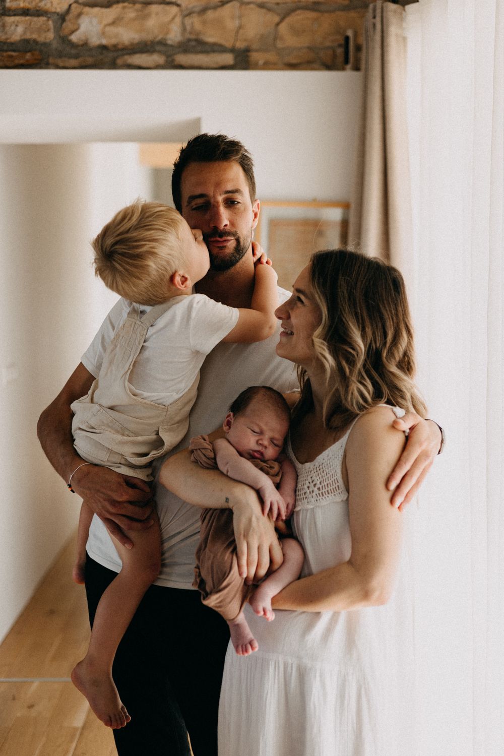 Portrait de famille intime montrant les parents avec leurs enfants dans un moment tendre près d'une fenêtre.