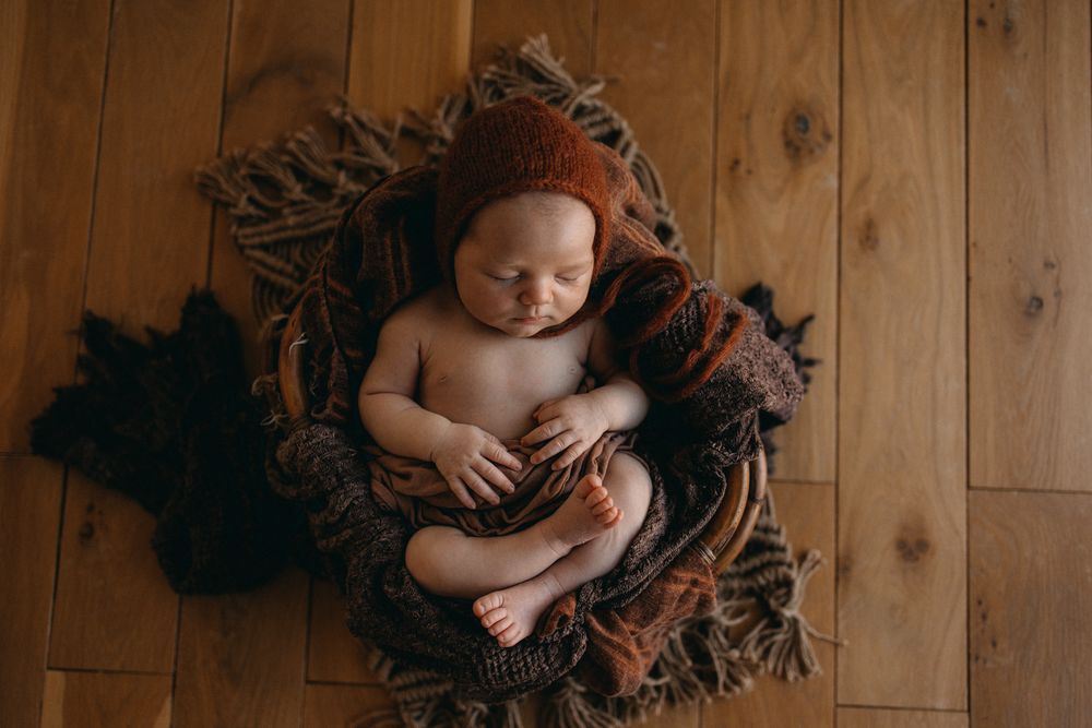 Portrait artistique de nouveau-né avec bébé dormant sur un sol en bois entouré de tissus texturés.