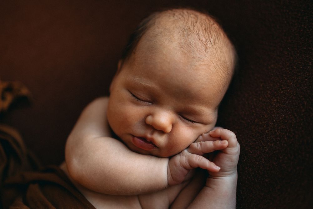 Peaceful sleeping newborn with hand tucked under cheek.