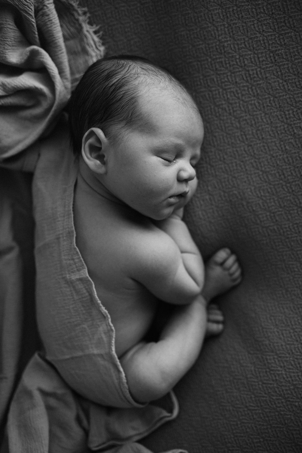 Portrait artistique en noir et blanc d'un nouveau-né endormi drapé dans un tissu doux.