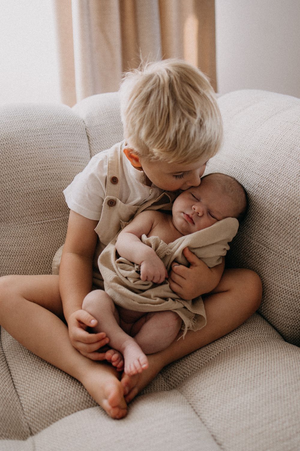 Tendre moment de frère et sœur sur le canapé alors que l'enfant plus âgé tient et embrasse un nouveau-né endormi.