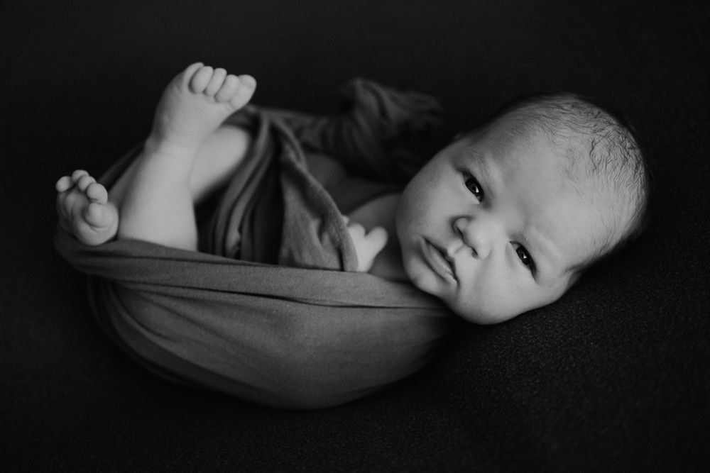 Black and white portrait of newborn wrapped in soft fabric.