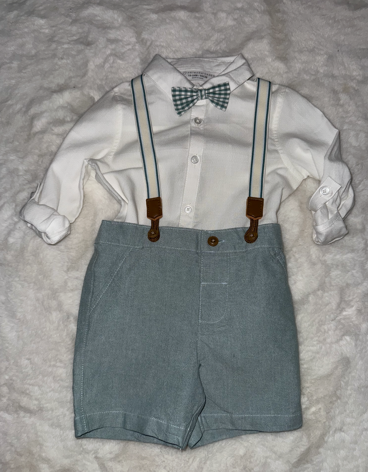 Gray shorts with white dress shirt and suspender attachments laid flat.