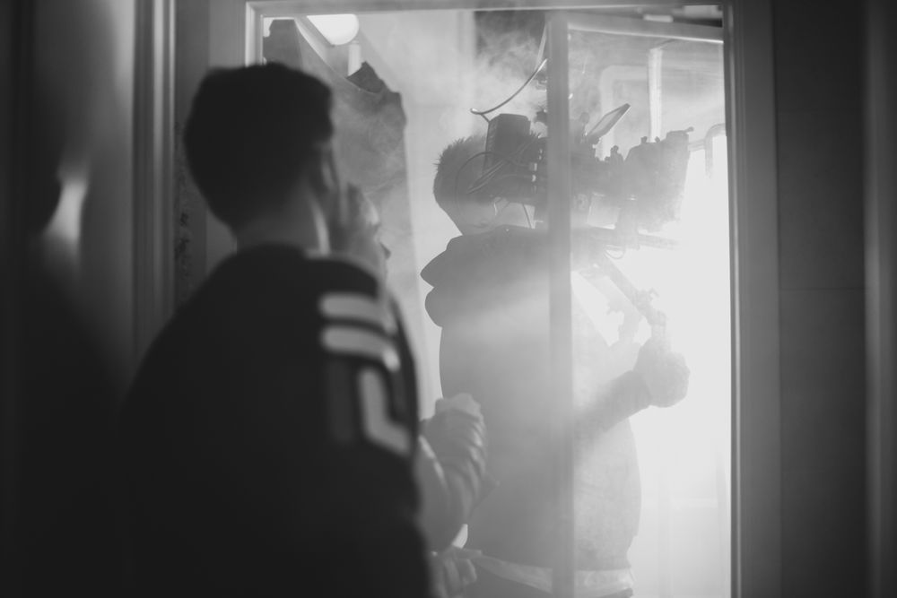 Cinematic black and white scene with silhouettes moving through backlit doorway.