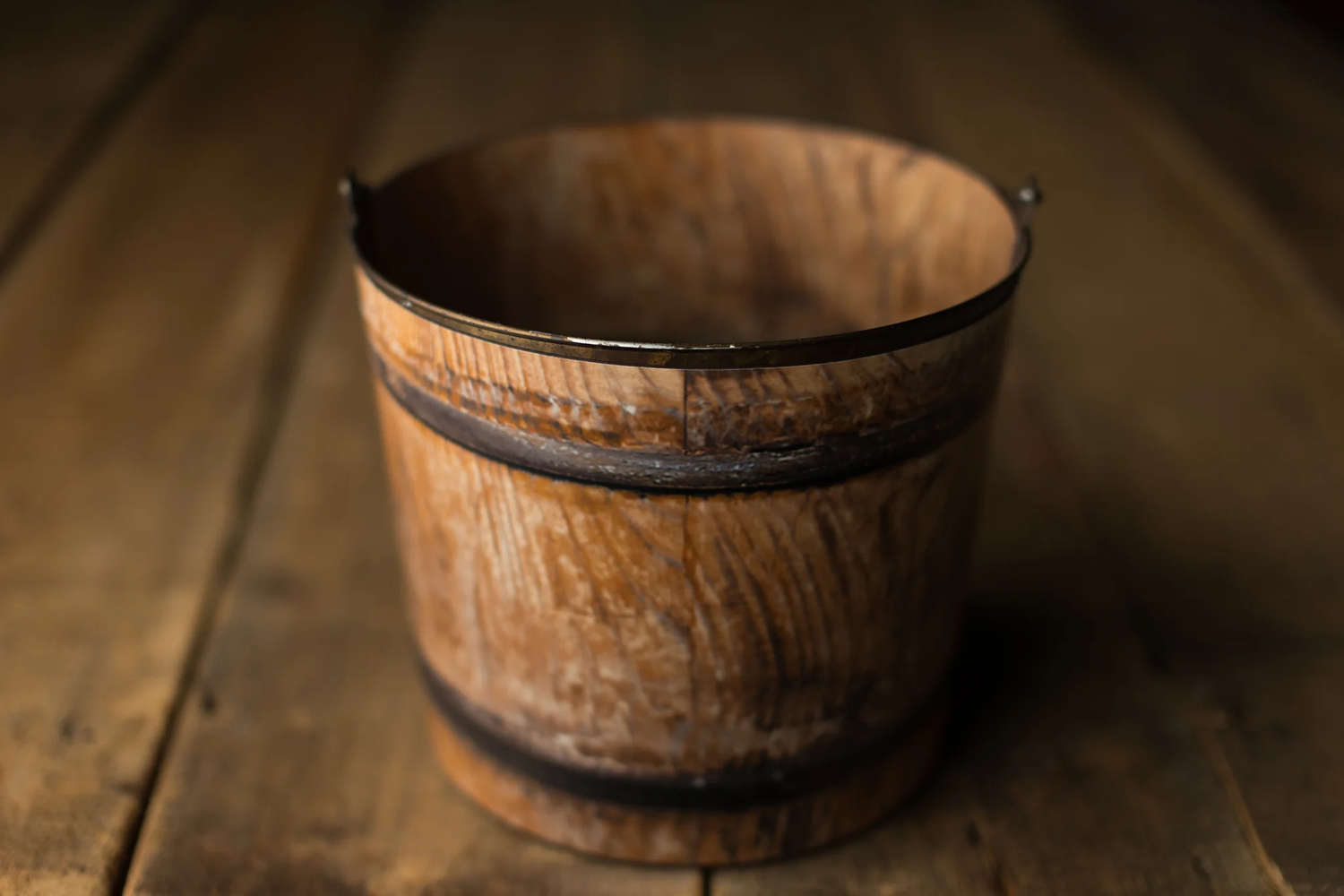 Rustic wooden barrel bucket with metal bands on aged wood floor.