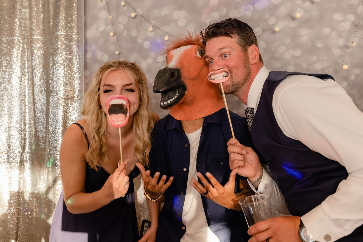 Wedding party guests pose with fun photo booth props against a sparkly backdrop at a reception.