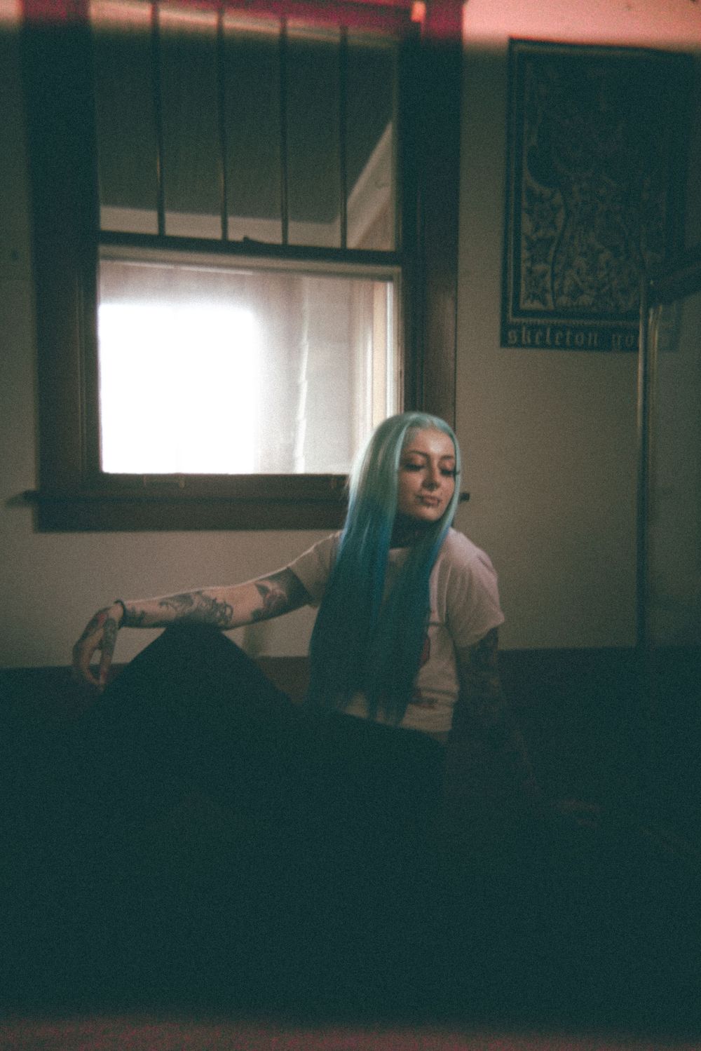 Moody indoor portrait with blue hair against dark background and window light.