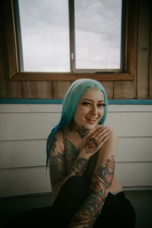 Natural window light portraits showing tattoos and teal hair in casual setting.